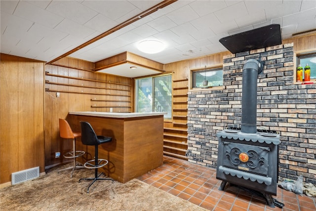 bar featuring a wood stove, dark tile patterned floors, wood walls, and brick wall