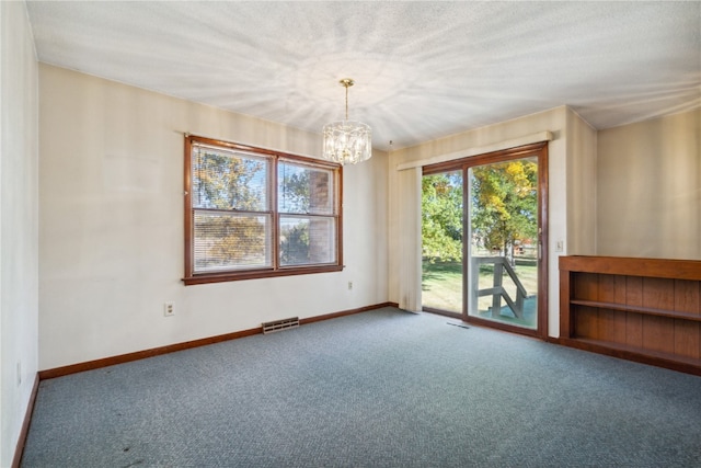 carpeted empty room with a notable chandelier and a textured ceiling