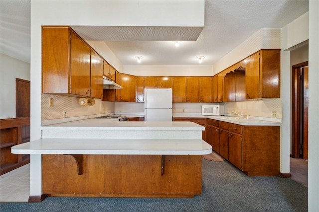 kitchen featuring carpet floors, white appliances, a breakfast bar area, and kitchen peninsula