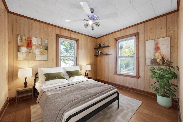 bedroom featuring wood walls, hardwood / wood-style flooring, multiple windows, and ceiling fan