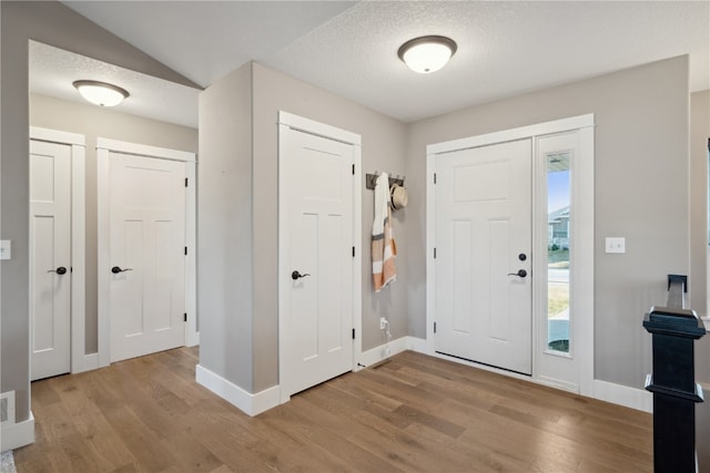 foyer entrance with vaulted ceiling, a textured ceiling, and light hardwood / wood-style floors