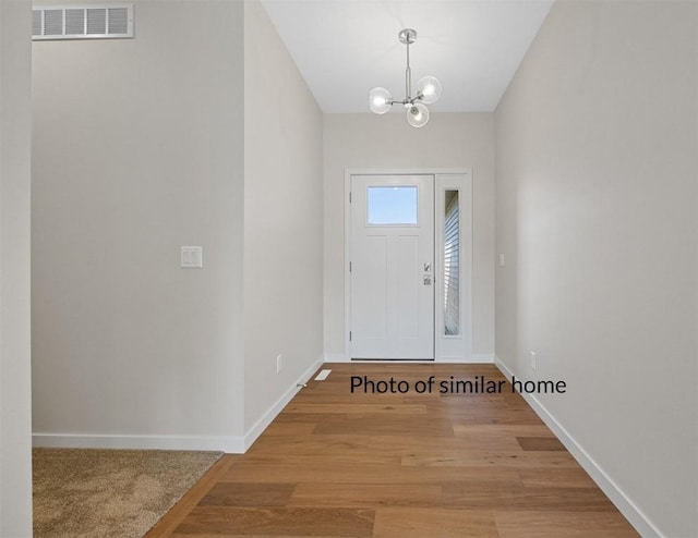 entrance foyer with a notable chandelier, light wood finished floors, visible vents, and baseboards