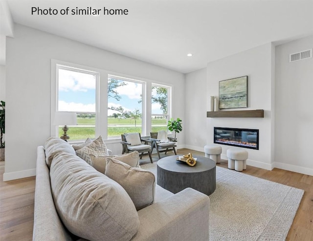 living room featuring recessed lighting, visible vents, a glass covered fireplace, light wood-type flooring, and baseboards