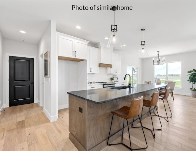 kitchen with a center island with sink, light wood-style floors, white cabinetry, a sink, and a kitchen breakfast bar