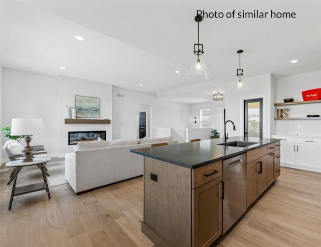 kitchen with a sink, stainless steel dishwasher, light wood-type flooring, dark countertops, and a glass covered fireplace