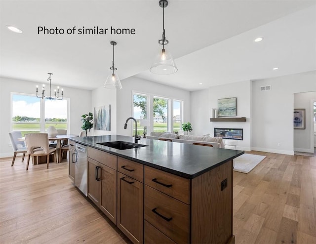 kitchen with dark countertops, stainless steel dishwasher, a sink, and a glass covered fireplace