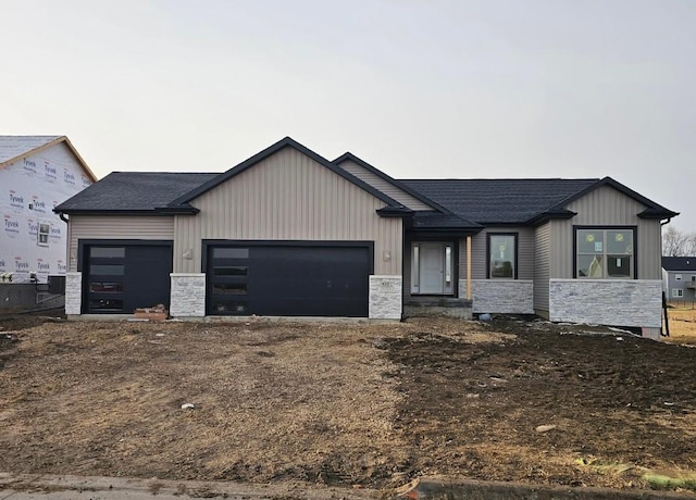 view of front of house featuring an attached garage, stone siding, and a shingled roof