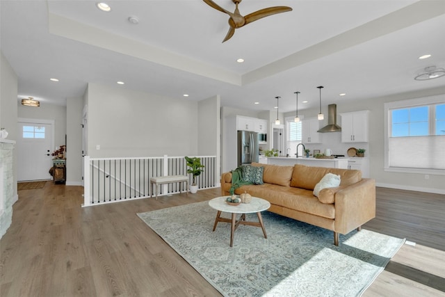 living room with light hardwood / wood-style floors, sink, a tray ceiling, and ceiling fan