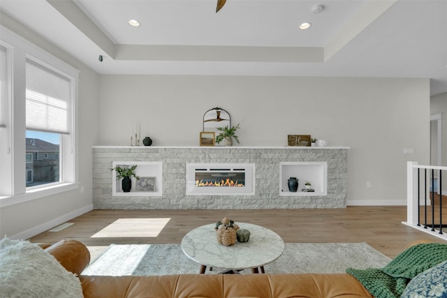 living room with a fireplace, a tray ceiling, and light wood-type flooring