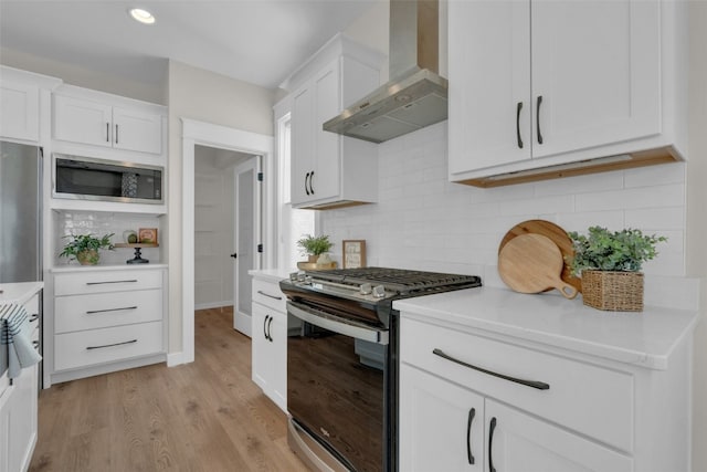 kitchen featuring light hardwood / wood-style flooring, wall chimney range hood, appliances with stainless steel finishes, and white cabinets