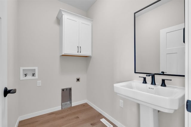 washroom featuring hookup for a washing machine, electric dryer hookup, light hardwood / wood-style floors, and cabinets