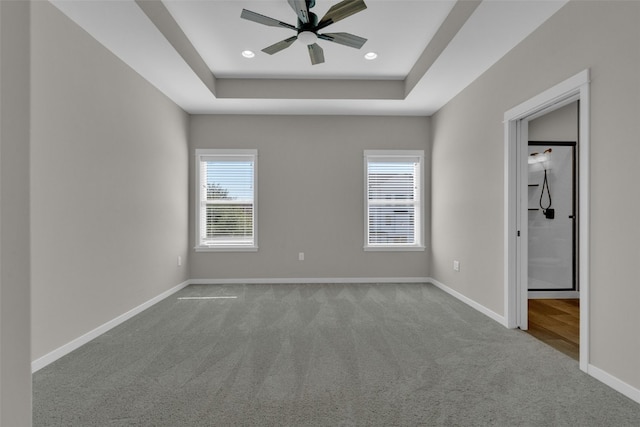 carpeted spare room with a raised ceiling and ceiling fan