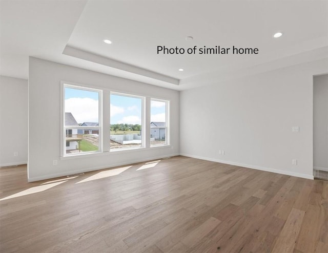 unfurnished living room featuring a raised ceiling and light hardwood / wood-style flooring