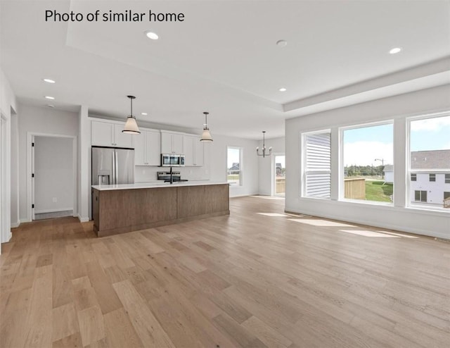 kitchen with hanging light fixtures, a large island, light hardwood / wood-style floors, white cabinetry, and stainless steel appliances