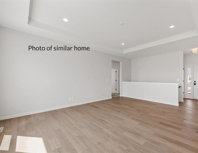 empty room with a raised ceiling and light hardwood / wood-style floors