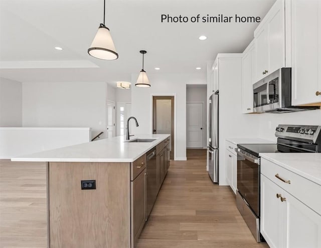 kitchen with sink, stainless steel appliances, decorative light fixtures, a kitchen island with sink, and white cabinets