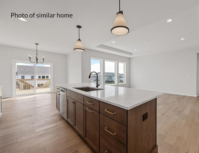 kitchen with a kitchen island with sink, hanging light fixtures, sink, light hardwood / wood-style flooring, and stainless steel dishwasher