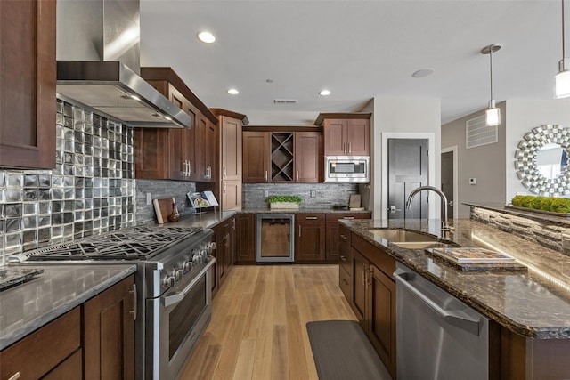 kitchen featuring wall chimney exhaust hood, wine cooler, sink, light wood-type flooring, and appliances with stainless steel finishes