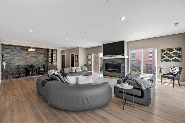 living room with a stone fireplace and light wood-type flooring