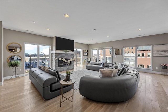 living room with light hardwood / wood-style floors, a stone fireplace, and plenty of natural light