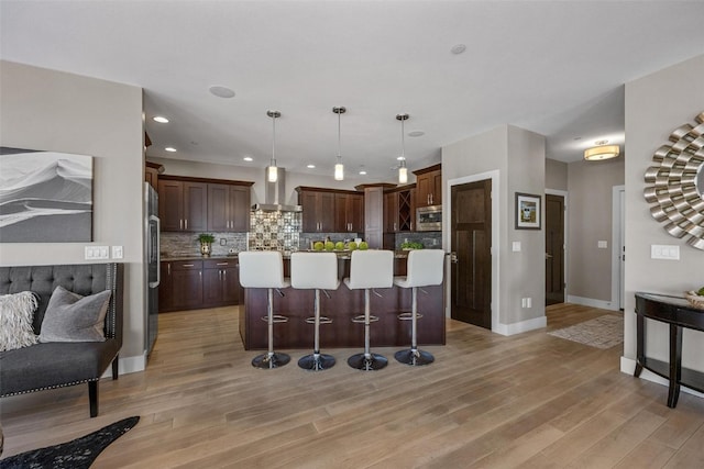 kitchen with wall chimney exhaust hood, decorative backsplash, hanging light fixtures, and light hardwood / wood-style floors