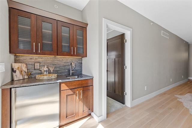 bar featuring tasteful backsplash, sink, light wood-type flooring, stainless steel fridge, and dark stone countertops