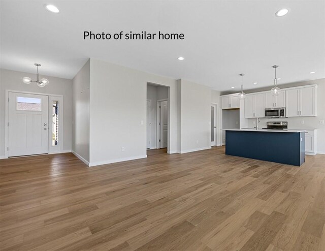 kitchen with light hardwood / wood-style flooring, white cabinets, a kitchen island with sink, and hanging light fixtures