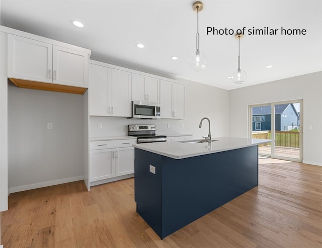 kitchen with white cabinetry, stainless steel appliances, decorative light fixtures, and a kitchen island with sink