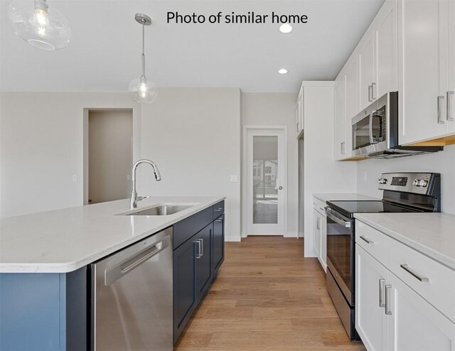 kitchen featuring appliances with stainless steel finishes, sink, white cabinetry, light hardwood / wood-style floors, and pendant lighting