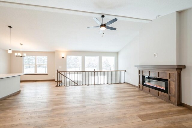 unfurnished living room with vaulted ceiling with beams, a tiled fireplace, ceiling fan with notable chandelier, and light hardwood / wood-style floors