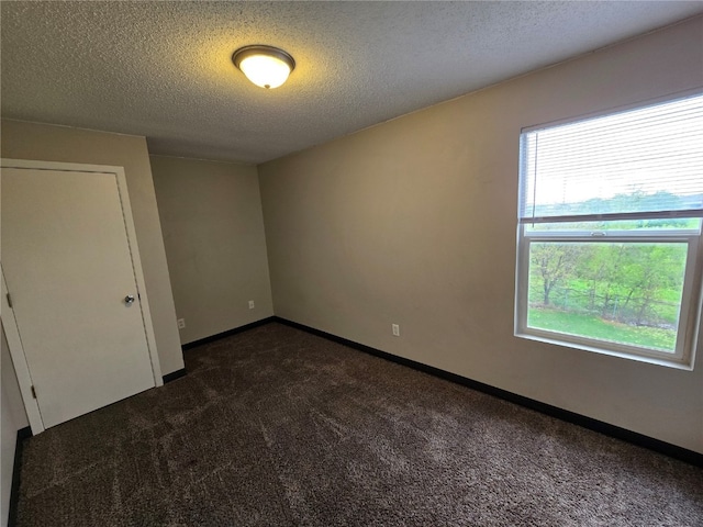 unfurnished room with dark colored carpet, a textured ceiling, and a wealth of natural light