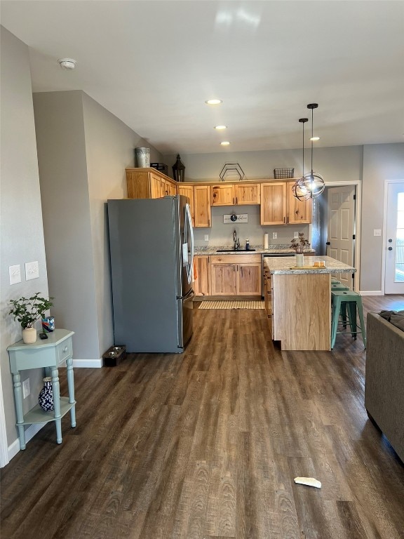 kitchen with light stone countertops, sink, stainless steel fridge, decorative light fixtures, and dark wood-type flooring