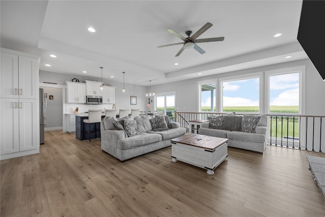 living room with ceiling fan with notable chandelier and light wood-type flooring