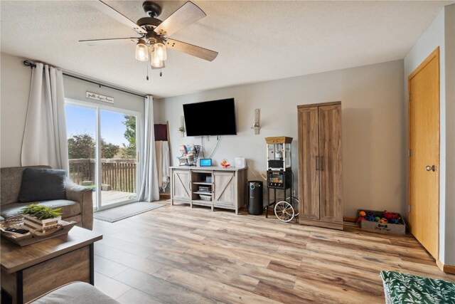 living room with a textured ceiling, light wood-type flooring, and ceiling fan