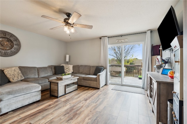 living room with a textured ceiling, light wood-type flooring, and ceiling fan