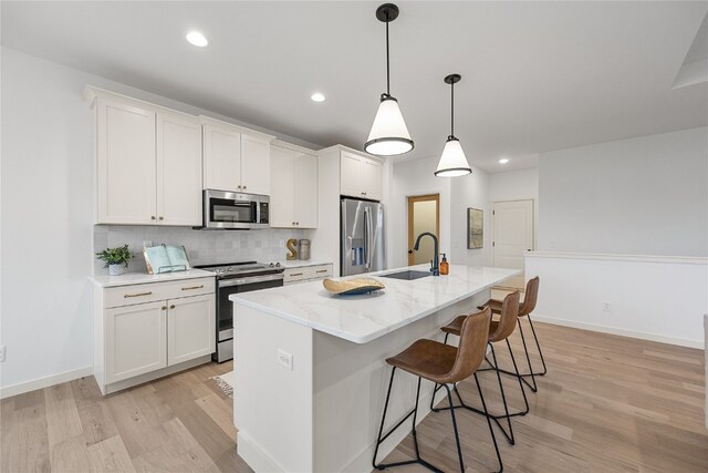 kitchen with appliances with stainless steel finishes, white cabinets, hanging light fixtures, and a center island with sink