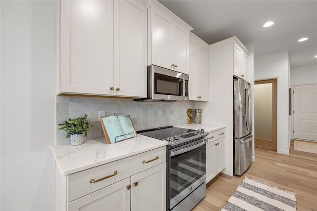 kitchen featuring backsplash, light stone countertops, white cabinetry, light wood-type flooring, and appliances with stainless steel finishes