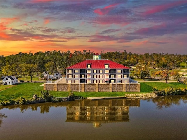 back house at dusk with a lawn and a water view