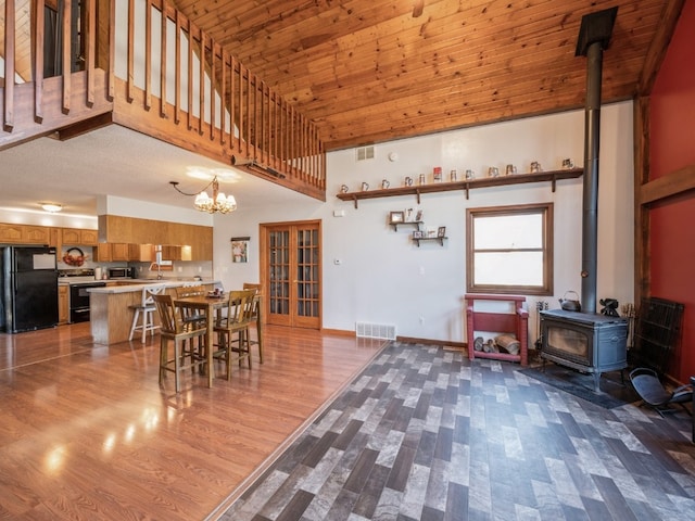 dining room with wood ceiling, a wood stove, wood-type flooring, and a high ceiling