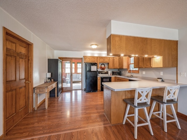 kitchen featuring kitchen peninsula, a breakfast bar area, appliances with stainless steel finishes, a textured ceiling, and light wood-type flooring