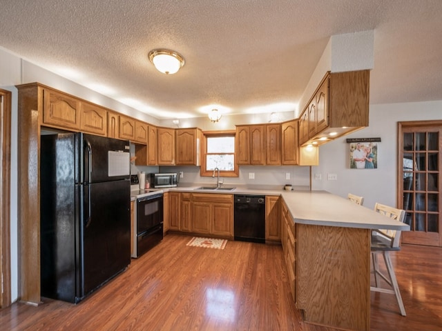 kitchen with kitchen peninsula, a breakfast bar, wood-type flooring, black appliances, and sink