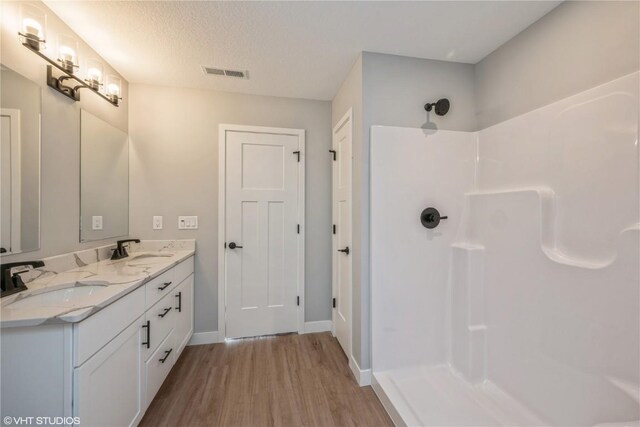 2734 Rookwood Ln, Marion, IA 52302 - bathroom with wood finished floors, a shower, baseboards, double vanity, and a textured ceiling
