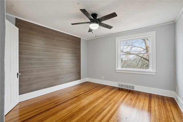 spare room featuring wooden walls, hardwood / wood-style flooring, ceiling fan, crown molding, and a textured ceiling