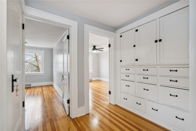 hallway with ornamental molding, a healthy amount of sunlight, and light hardwood / wood-style flooring