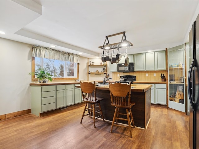 kitchen with wooden counters, black appliances, light wood-type flooring, and an island with sink