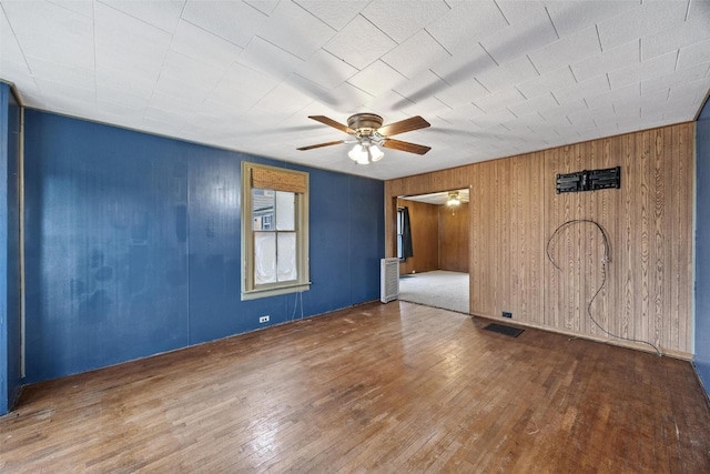 spare room with ceiling fan, hardwood / wood-style flooring, and wood walls