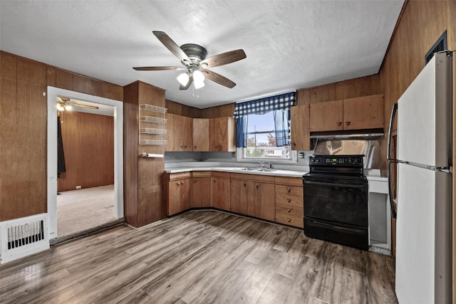 kitchen featuring wooden walls, light hardwood / wood-style flooring, sink, black / electric stove, and white refrigerator