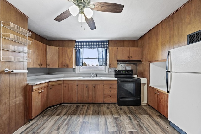 kitchen featuring dark hardwood / wood-style flooring, wood walls, white fridge, black range with electric cooktop, and sink