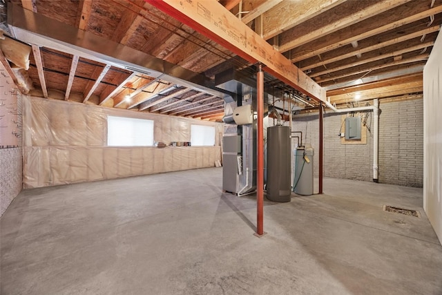 basement featuring electric panel, heating unit, gas water heater, and brick wall