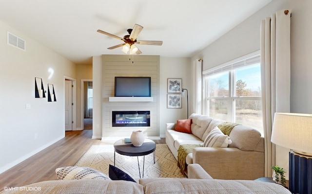 living room featuring light hardwood / wood-style floors, a large fireplace, and ceiling fan